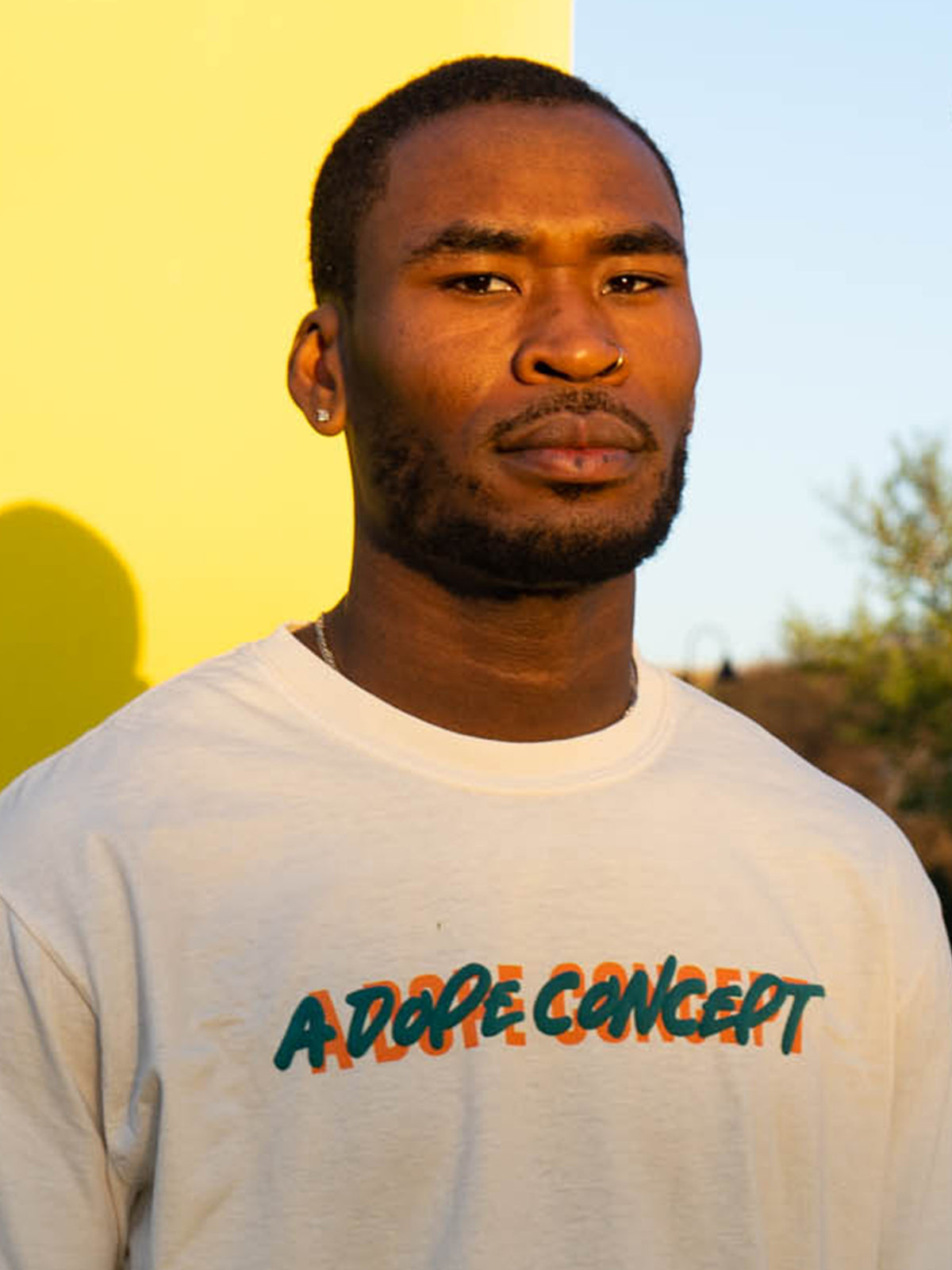A person wearing a white ADC logo tee with a flat print under and puff print on top, standing in front of a yellow background.